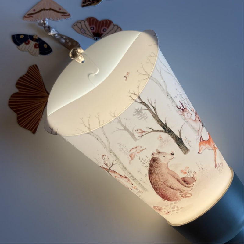 Focus sur la collerette de la lampe nomade. On distingue les détails du motif de forêt enchantée avec un ours assis sur le sol face à un faon.