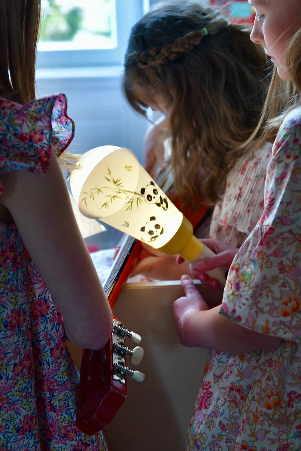 Nous voyons 3 petites filles rassemblées avec l'une d'entre elles qui tient la lampe nomade panda allumée dans sa main