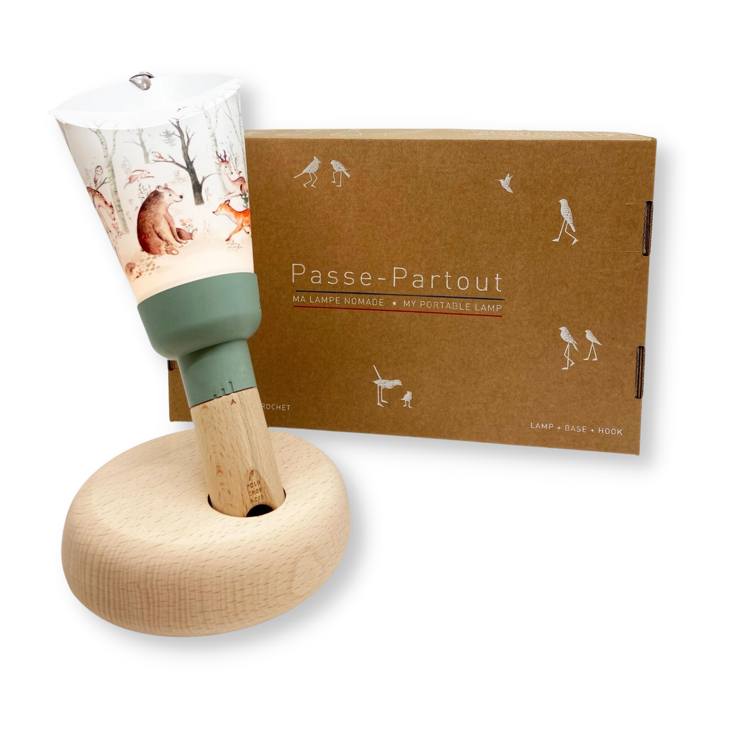 La lampe nomade est posée sur son socle en bois. Il s'agit d'une lampe facilement préhensible pour les enfants avec un manche en bois et une collerette arborant des motifs, ici un motif de forêt avec des animaux aux allures douces et poétiques tels qu'un ours, un cerf, un hérisson.