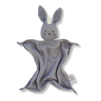 Doudou lapin en coton bio gris avec de longues oreilles et des noeuds au bout des pattes. Il a de petits yeux brodés noir, trois traits de moustache noire de chaque côté de son petit nez en forme de coeur.