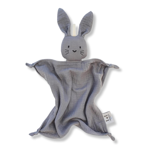 Doudou lapin en coton bio gris avec de longues oreilles et des noeuds au bout des pattes. Il a de petits yeux brodés noir, trois traits de moustache noire de chaque côté de son petit nez en forme de coeur.