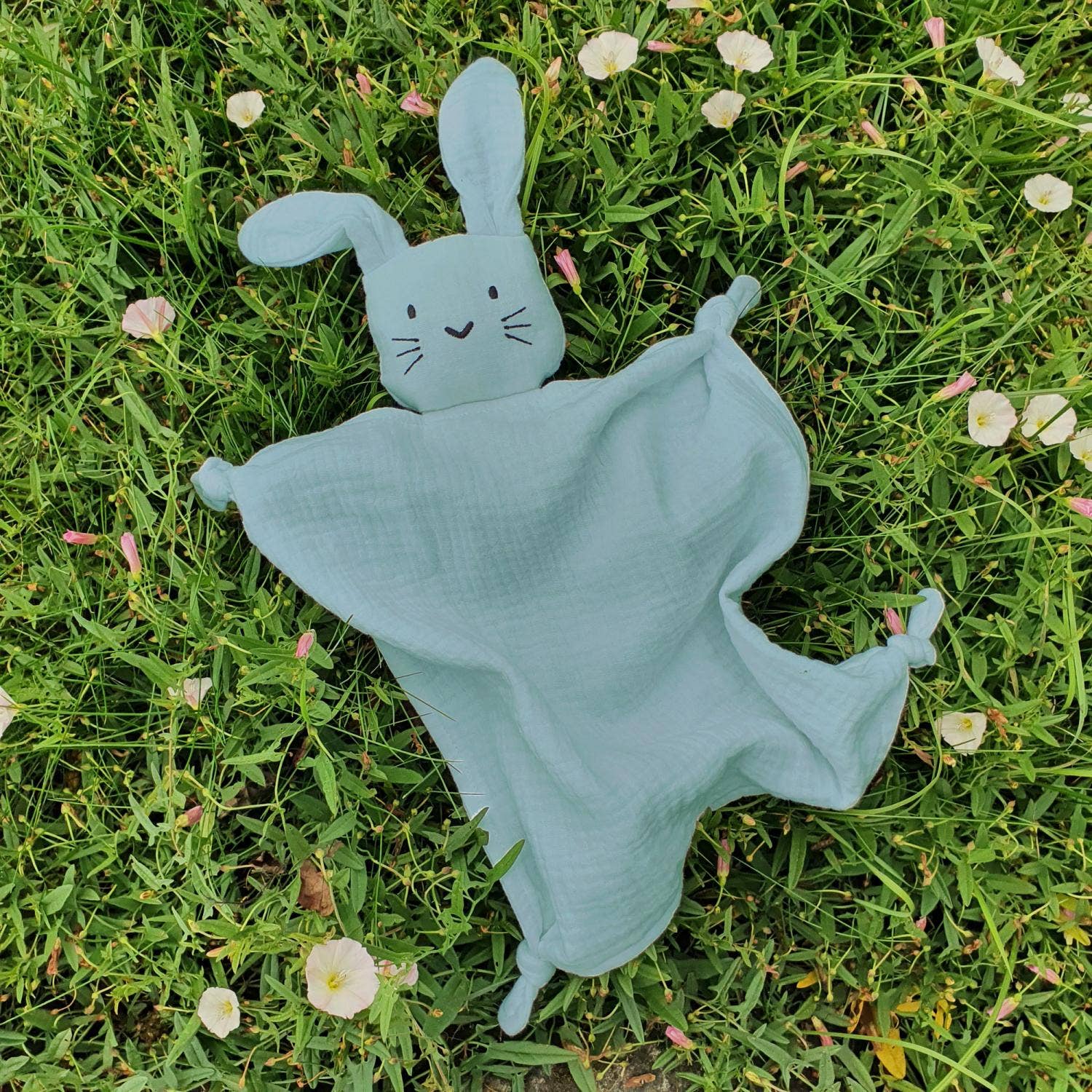 Doudou lapin vert posé dans l'herbe entouré de fleurs de printemps