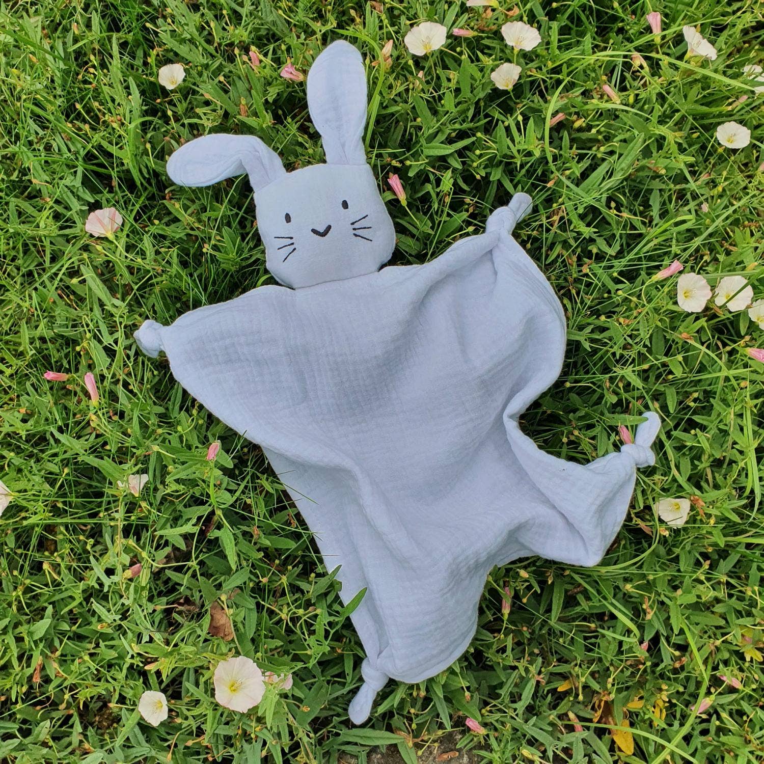 Doudou lapin gris dans l'herbe fraiche entouré de fleurs de printemps.