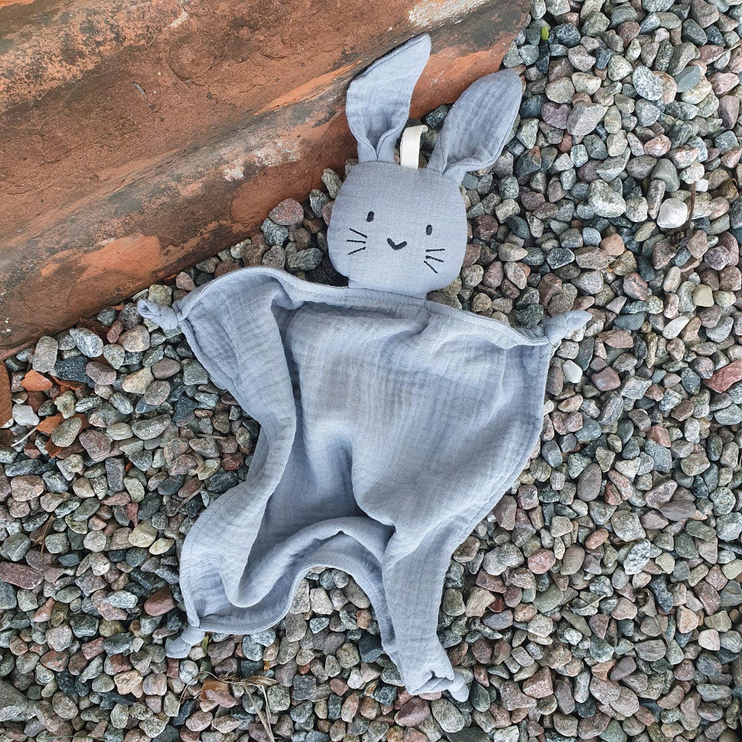 Doudou lapin gris posé sur les graviers.