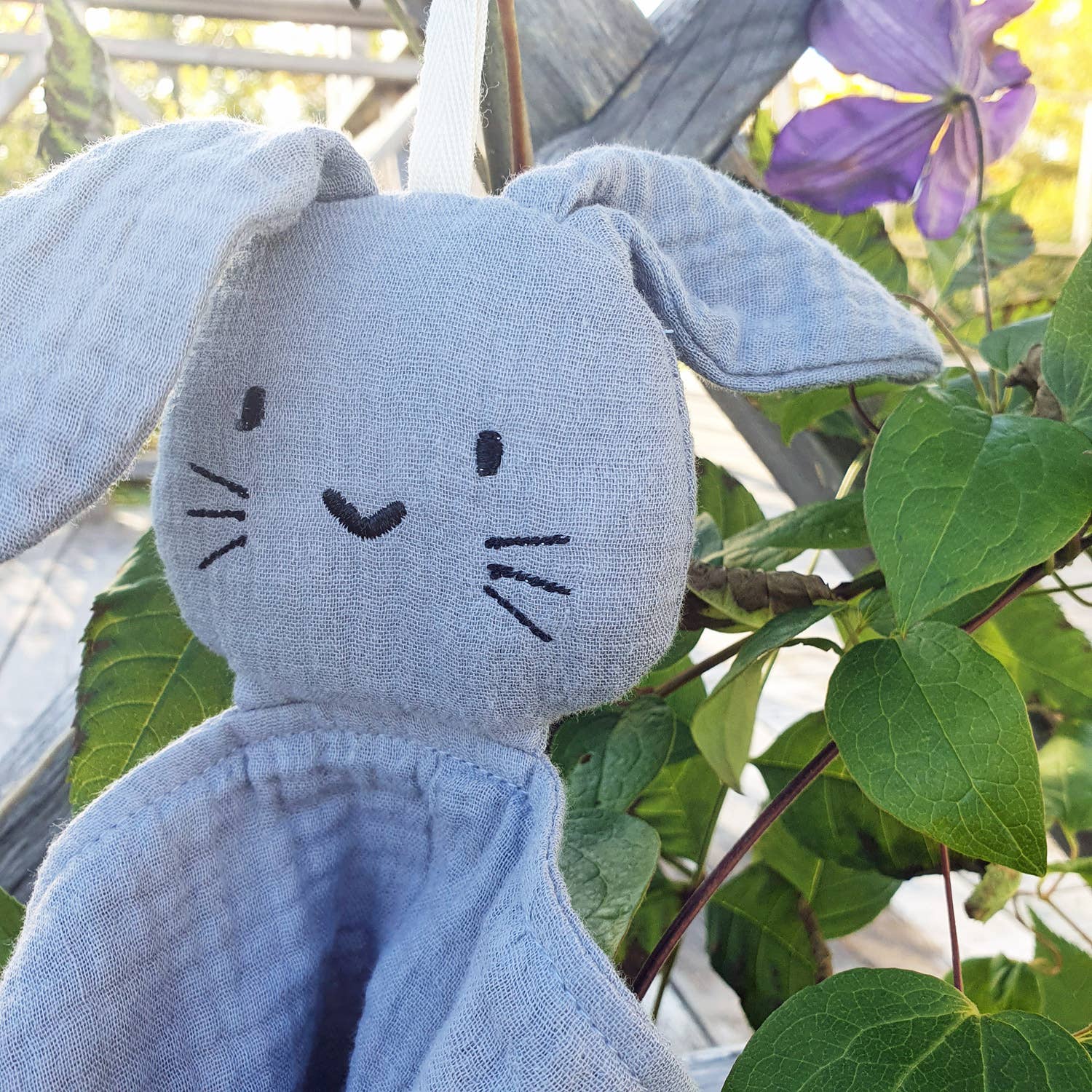 doudou lapin gris zoomé sur son visage, entouré de plantes vertes.