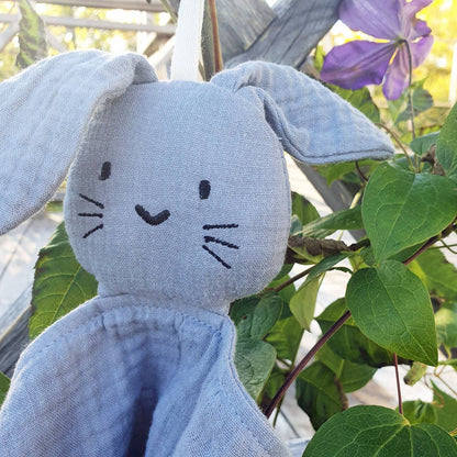 doudou lapin gris zoomé sur son visage, entouré de plantes vertes.