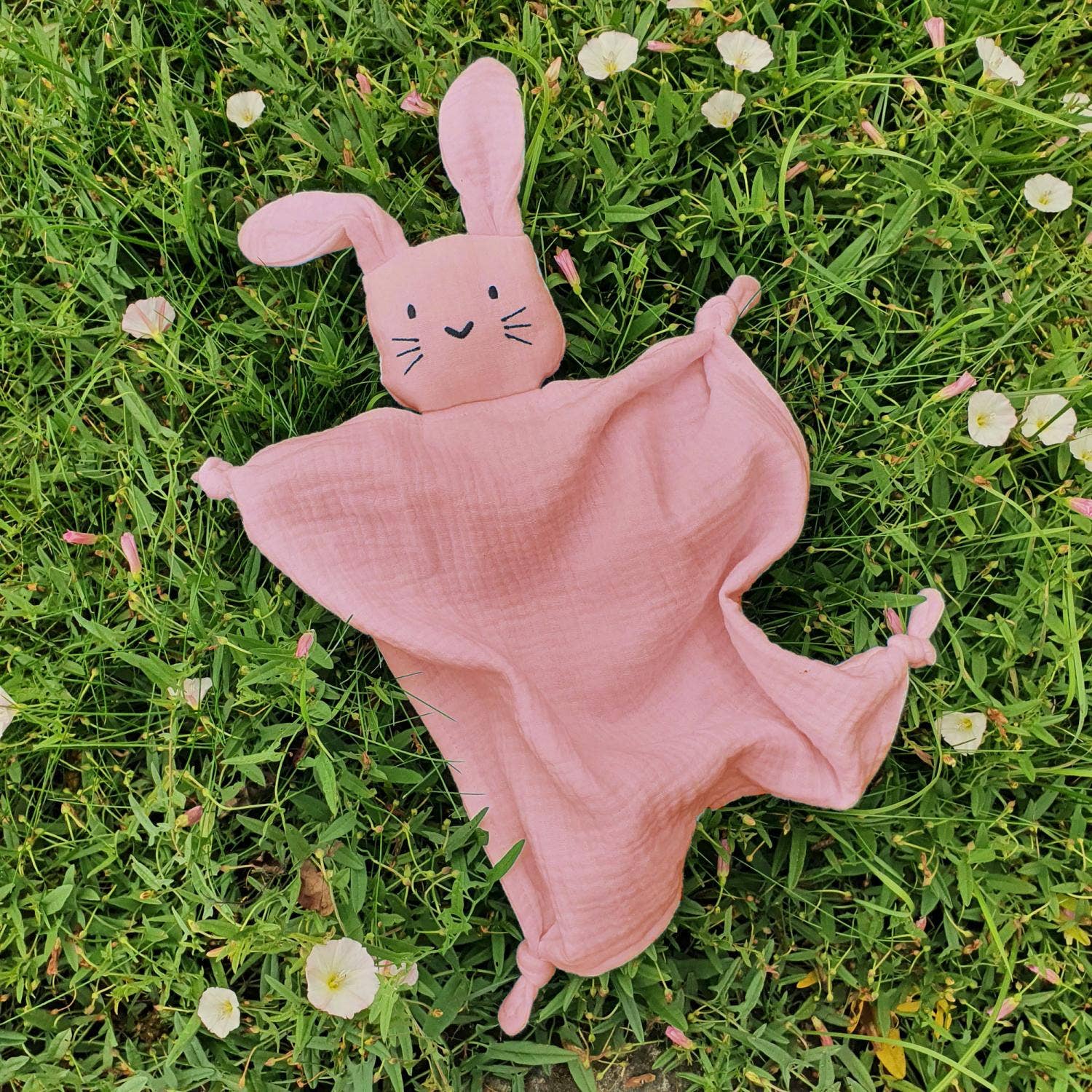 Un doudou lapin en coton bio rose posé dans l'herbe.