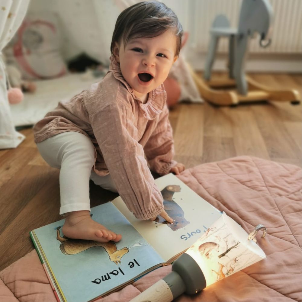 un jeune enfant est en train de regarder un livre avec sa lampe nomade allumée posée sur le sol à côté de lui.